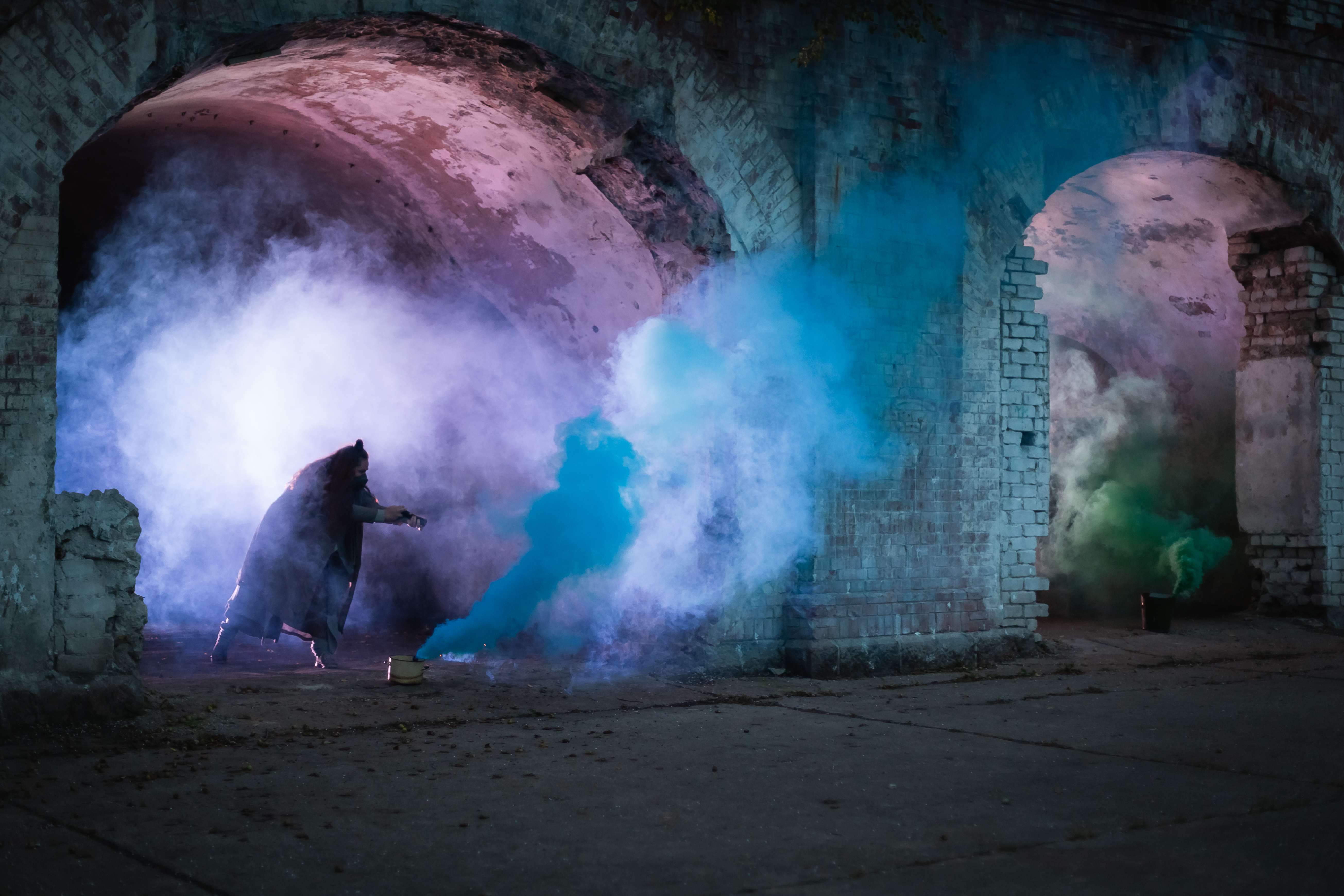 Blue smoke fills a railway arch, a person stands in the midst
