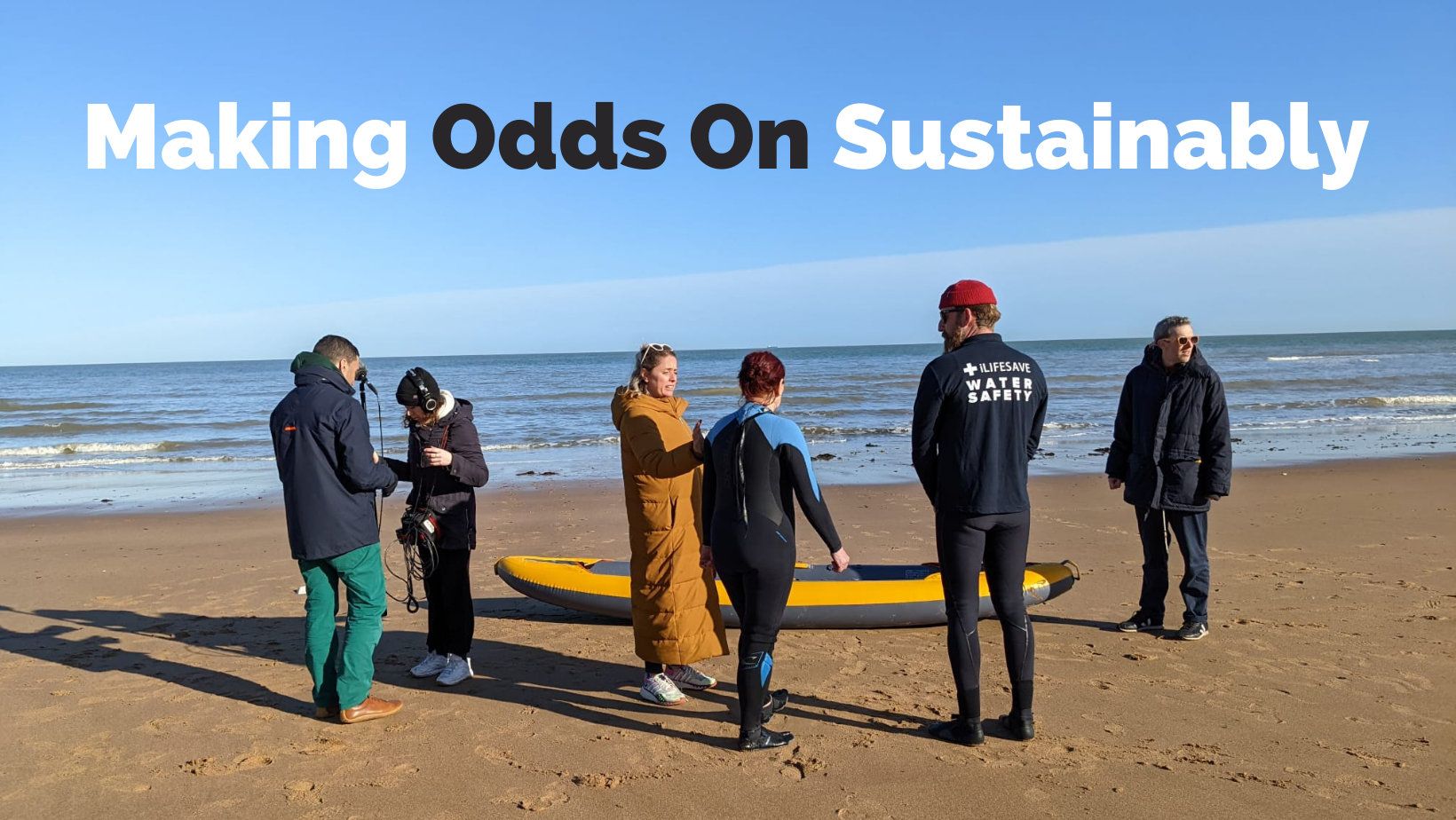 6 people stand on a beach, with a kayak and the sea behind them