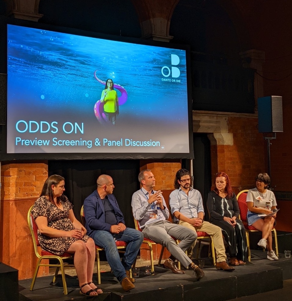 5 panellists and host sat on stage with the Odds On image on screen behind them with text ‘Odds On Preview Screening and Panel discussion’