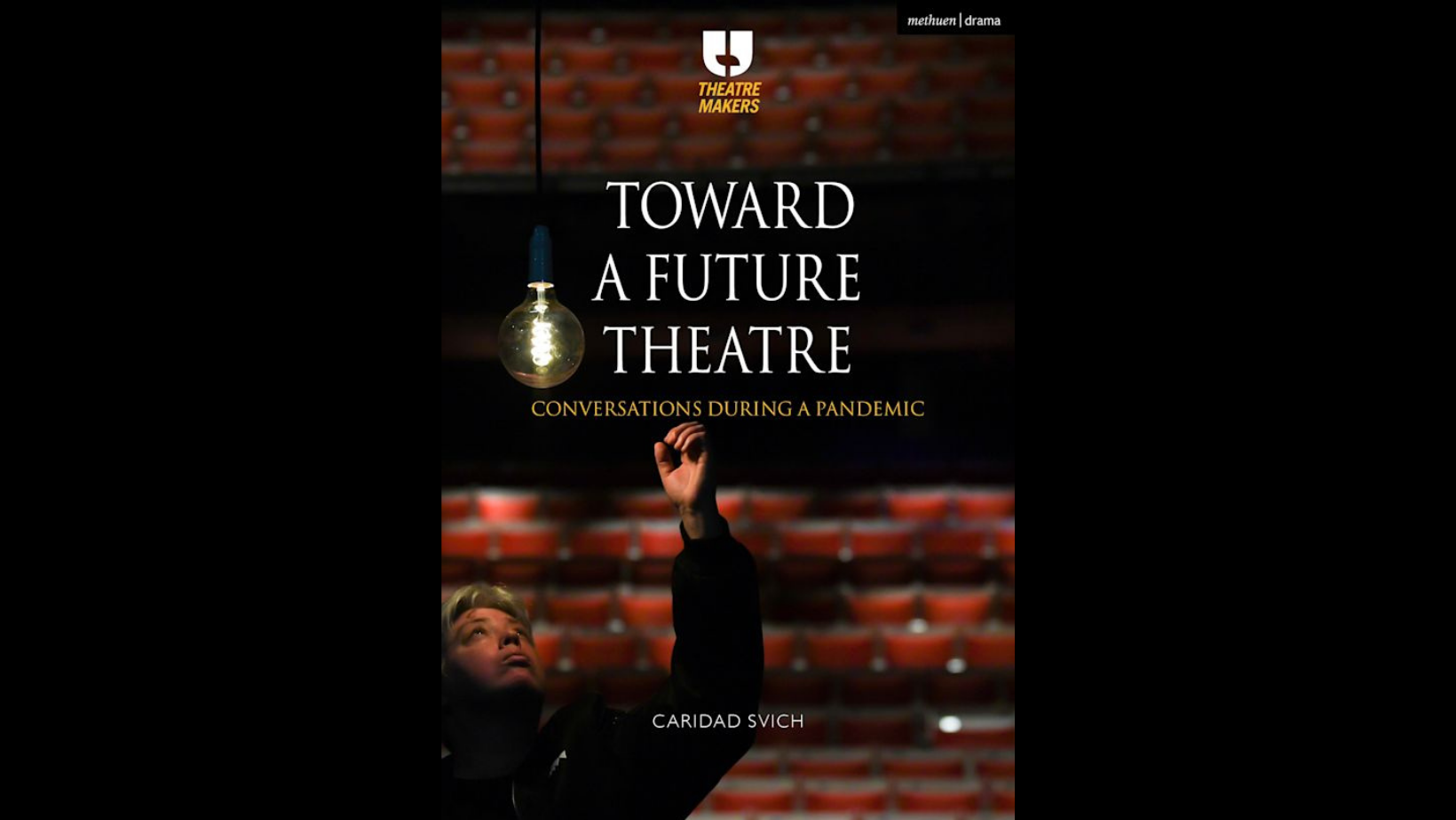 A dark theatre with red seats & a woman with her fist raised